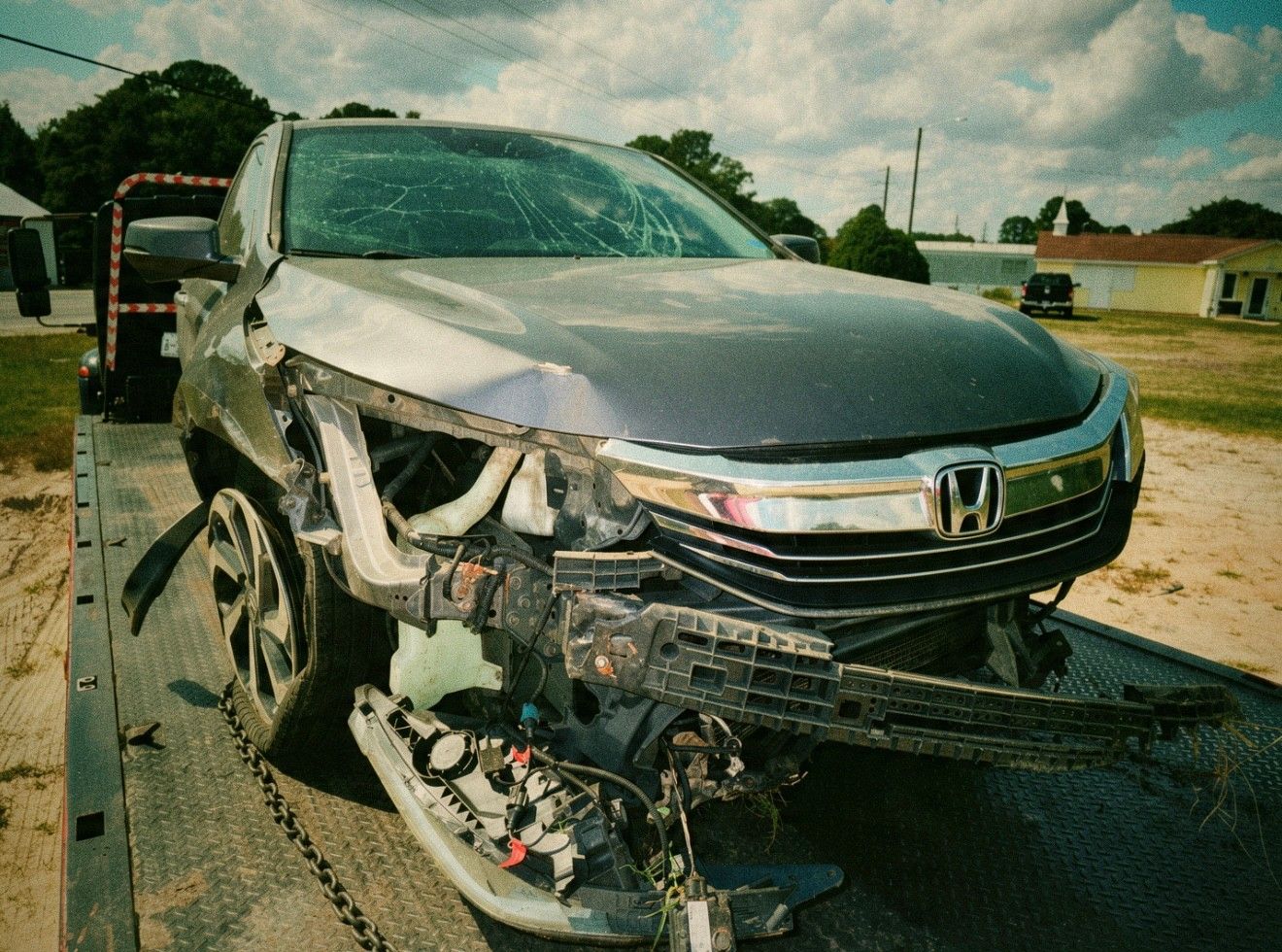 Gray 2016 Honda Accord with heavy front-end collision damage and a cracked windshield, strapped to a rollback tow truck